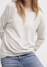 Ljusbeige tröja med avslappnad passform, långa ärmar och ribbade detaljer vid ärmsluten. Det mjuka tyget har en något strukturerad yta.