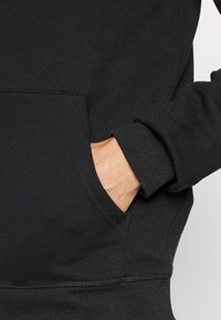 Zwarte hoodie van een katoenmix heeft een voorzak en ribgebreide manchetten. De textuur lijkt zacht met minimale zichtbare vezels.