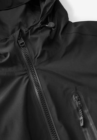 Veste imperméable noire avec col montant, capuche réglable et fermeture éclair frontale avec rabat protecteur. Comprend des poches latérales zippées.