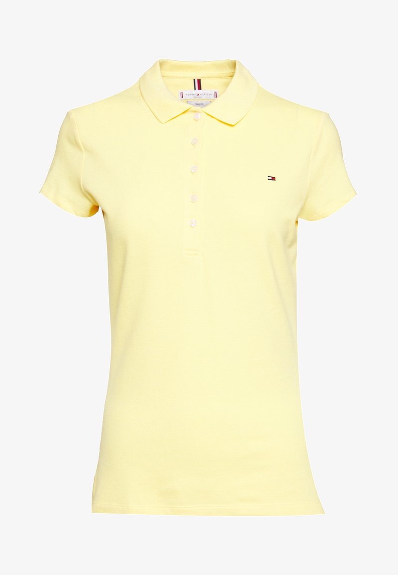 Polo jaune clair à manches courtes avec col et six boutons blancs, présentant un petit logo Tommy Hilfiger sur la poitrine gauche.