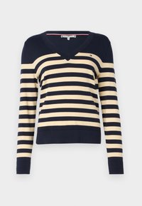 Sweter w paski w kolorze ciemnego granatu i kremowym. Posiada dekolt w serek, długie rękawy oraz ściągacz na dole. Materiał wydaje się gładki i lekki.