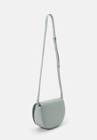 Světle modrá crossbody taška s zakřiveným tvarem, hladkým matným povrchem, nastavitelným popruhem a subtilními kovovými detaily.