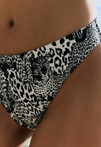 Bikiniji spodnji del v črno-belem leopardjem vzorcu z srednjim rezom, ki vsebuje podrobne živalske vzorce na gladkem, raztegljivem materialu.