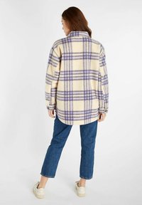 Fleece shirtjack met een geel- en paarsgeruite print, met kraag en knoopmanchetten. Gecombineerd met blauwe denim en witte sneakers.