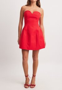 Robe rouge sans bretelles avec un décolleté en cœur et une jupe évasée. Fabriquée en tissu lisse, elle présente des lignes épurées et des accents minimaux.