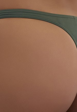 Green fabric bikini bottom with a smooth texture, featuring a narrow waistband and seamless design, set against a warm skin tone background.