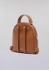Kožený batoh v barvě tan s zaobleným tvarem, dvojitými horními rukojeťmi a nastavitelnými bočními popruhy. Obsahuje stříbrný zip a detail s kovovým štítkem.