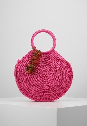 Sac à main tissé rond rose avec poignées circulaires et trois décorations pompons multicolores suspendues à une poignée.