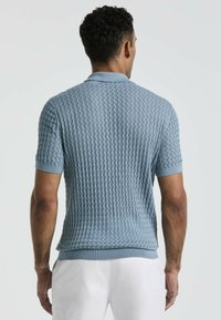 Blauwe polo met korte mouwen, voorzien van een gestructureerd patroon, ribbelkraag en manchetten. Het ontwerp is slim-fit met een subtiele, driedimensionale uitstraling.