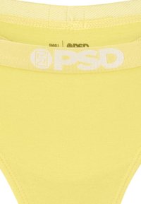 Keltaiset PSD alusvaatteet, joissa on sileä pinta ja brändätty joustovyö. Koko-etiketti osoittaa pienen koon. Yksinkertainen malli ilman kuvioita.