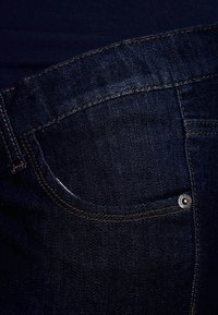 Tmavě modré džíny z denimu s přední kapsou s výrazným šitím, kovovou cvočkem a hladkou texturou.