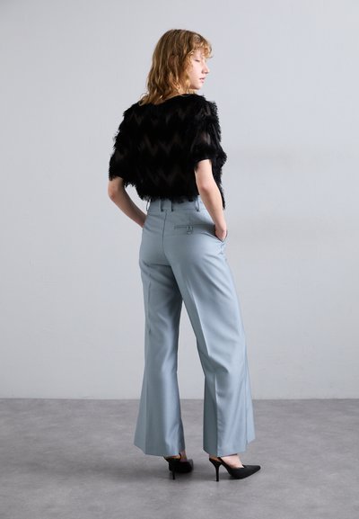 Czarny włochaty krótki top z teksturą w zygzak, połączony z jasnoniebieskimi spodniami o szerokich nogawkach i czarnymi szpilkami z ostro zakończonym noskiem.