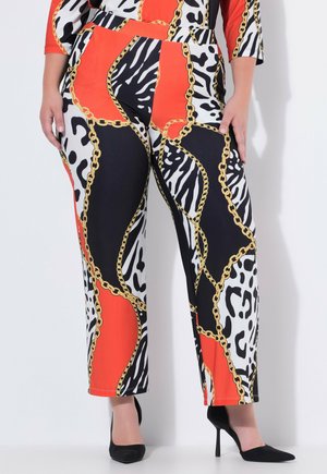 Leggingsit, joissa on rohkeita mustia, valkoisia ja punaisia eläinkuosisia paloja, päällekkäin kultakuvioisten ketjujen kanssa, yhdistetty mustiin korkeakorkoisiin kenkiin.