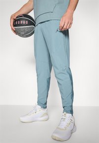 Light blue athletic pants with a slim fit and tapered legs, paired with white sneakers. Black and gray basketball held in one hand.