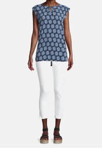 Námořnická modrá bezrukávová tunika s bílým vzorem listů, s výstřihem ve tvaru klíče. Slučuje se s přiléhavými bílými kalhotami a černými platformovými sandály.