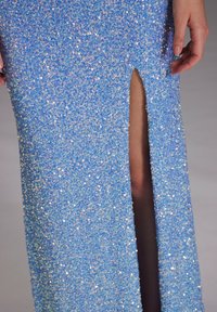 Robe bleue pailletée avec une fente haute, présentant une texture scintillante et une silhouette ajustée qui met en valeur les jambes.