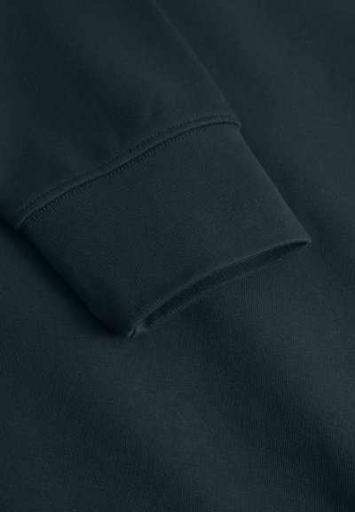 Poignet de sweat-shirt vert foncé, fabriqué en tissu doux mélangé coton. Présente une texture côtelée et des coutures contrastantes, avec un gros plan de la manche.