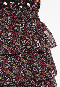 Vestido negro floral con volantes en capas. La tela es ligera y presenta una mezcla de flores en tonos rosa, rojo y amarillo sobre un fondo oscuro.