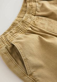 Shorts bej din bumbac cu talie elastică, dotate cu buzunare laterale, cusături fine și o textură netedă.