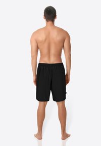 Schwarze Badehose mit elastischem Bund, einfachem Design, ohne Muster und einer einzelnen Gesäßtasche. Sicht von hinten.