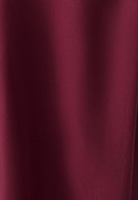 Tessuto bordeaux con una texture liscia, caratterizzato da una leggera lucentezza. Il materiale appare leggero, uniforme e privo di motivi o accessori visibili.