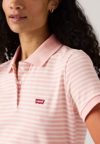 Polo in rosa chiaro con strisce bianche, maniche corte e colletto. Presenta una toppa rossa del logo Levi's sul lato sinistro del petto.