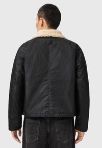 Chaqueta negra de tela texturizada con un cuello de borrego beige. Presenta un corte recto, costura en la parte posterior y etiqueta en el cuello.