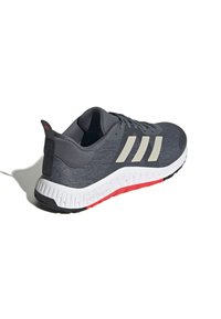Gray athletic shoe with knit upper, white midsole, red outsole, and three white stripes. Features a padded collar and textured detailing.