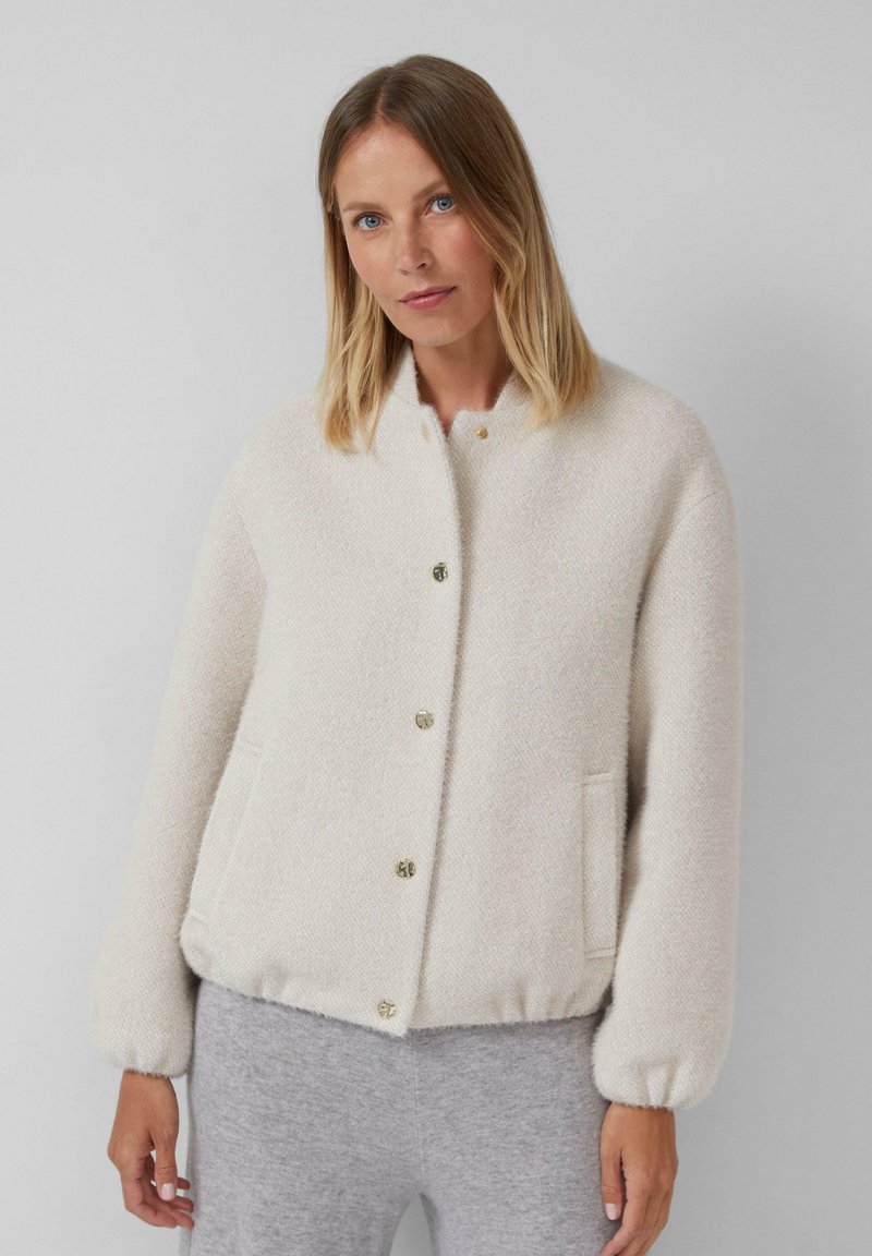 Texturierte cremefarbene Jacke mit rundem Ausschnitt, goldenen Knöpfen und elastischen Bündchen. Verfügt über Seitentaschen und ein lässiges Design.