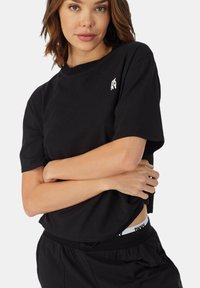 Czarny bawełniany t-shirt o luźnym kroju, z krótkimi rękawami i małym białym logo na piersi. W połączeniu z czarnymi spodniami ze sznurkiem.