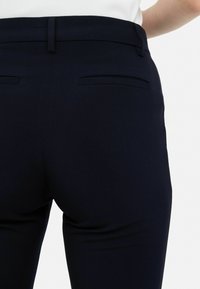 Pantalones ajustados azul marino con una textura suave, que incluyen bolsillos traseros y un diseño entallado, destacando una silueta limpia y estructurada.