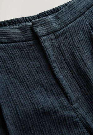Tela texturizada de color azul oscuro con un diseño arrugado. Presenta una cinturilla elástica y un cierre frontal plano con un detalle de pliegue.