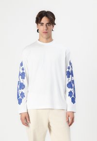 Witte langemouwen shirt van katoen, met een blauw bladerenpatroon op de mouwen, ronde halsontwerp en een ontspannen pasvorm.
