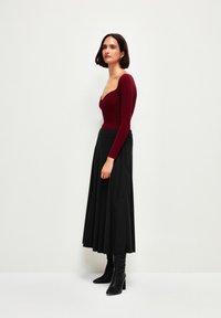 Haut côtelé bordeaux à manches longues avec un décolleté rond, associé à une jupe plissée noire et des bottes noires à talons hauts jusqu'aux genoux.