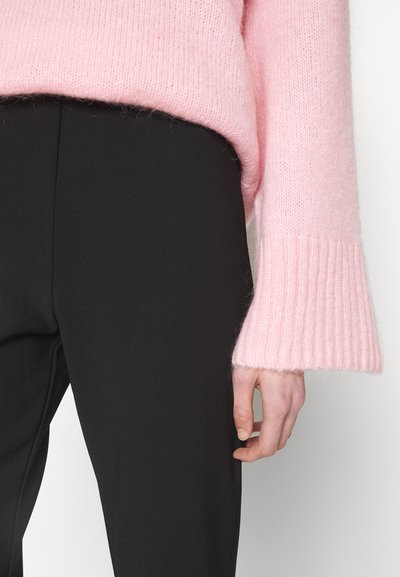 Light pink knitted sweater with ribbed cuffs, paired with black fitted trousers. Sweater features a soft, fuzzy texture.
