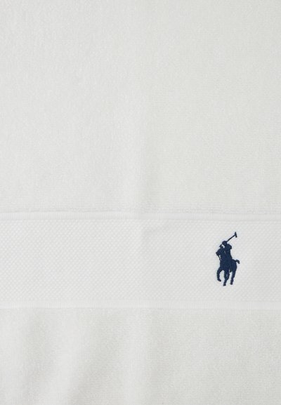Tela blanca texturizada con una banda horizontal que presenta un pequeño logo bordado de un jugador de polo en azul oscuro.