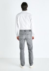 Jeans gris à coupe droite, avec des poches arrière et une ceinture. Assortis à une chemise blanche à rayures à manches longues. Baskets blanches.