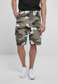 Shorts cargo camouflage en nuances de vert, noir et blanc, avec un tissu texturé, des poches avant et des poches cargo latérales.