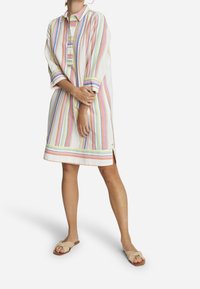 Randig klänning med krage i lätt tyg med pastellfärger (rosa, grön, blå) och sidoflikar; bärs med lätta platta sandaler.