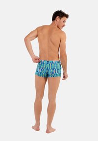 Badeshorts mit blauem Grundton und grünen, gelben und weißen Blattmustern. Aus dehnbarem Material gefertigt, mit enger Passform und ohne sichtbare Logos.