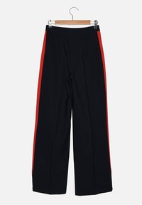 Pantalons larges noirs avec une bande latérale rouge, fabriqués dans un matériau lisse. Comprend des plis à l'avant et un cintre en bois.