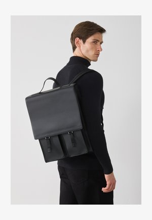 Zaino in pelle nera con design strutturato, caratterizzato da una chiusura a pattina e due tasche frontali. Texture liscia con spallacci regolabili.