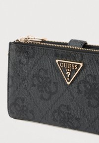 Musta teksturoitu lompakko synteettisestä materiaalista, jossa on kultasävyinen kolmionmuotoinen logo ja kaksoisvetoketjulla varustettu suljin.