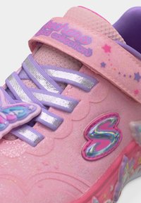 Ροζ παιδικό αθλητικό παπούτσι Skechers με μωβ κορδόνια, λαμπερό λογότυπο "S", σχέδια αστεριών και ένα κλιπ πεταλούδας στη γλώσσα.
