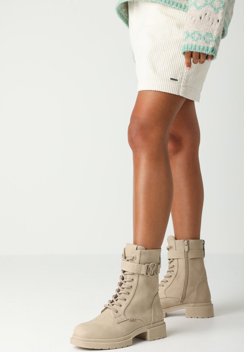 Beige snöre ankle boots med en kraftig sula, tillverkade av mocka, med dekorativa metalldetaljer och en sidodragkedja för enkel påtagning.