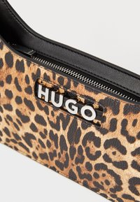 Borsa leopardata realizzata in materiale sintetico testurizzato, caratterizzata da una zip nera, dettagli in pelle nera e un logo "HUGO" bianco.