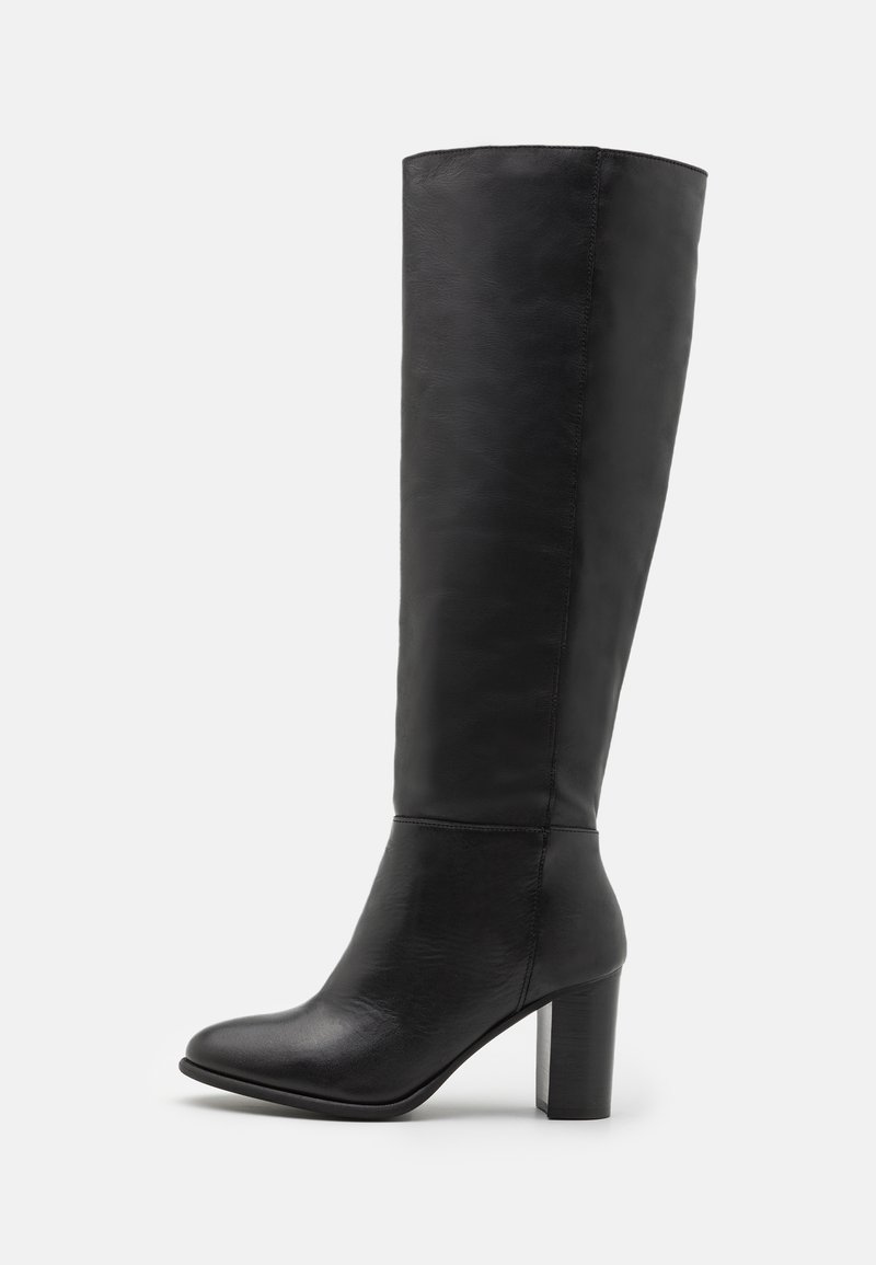 Bottes en cuir noir montant jusqu'au genou avec une texture lisse, un bout arrondi et un talon bloc épais. Coutures décoratives le long des côtés.