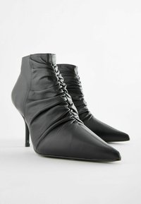 Černé kožené kotníkové boty s špičatou špičkou. Obsahují nabíranou texturu na svršku a štíhlé stiletto podpatky. Hladký povrch.