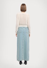 Jasnoniebieska długa spódnica dżinsowa z tylnymi kieszeniami, wysokim stanem i prostą sylwetką, zestawiona z kremowym swetrem dzianym z otwartym splotem.