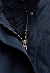 Close-up of a partially unzipped navy blue jacket with silver zipper and black mesh lining visible inside.
